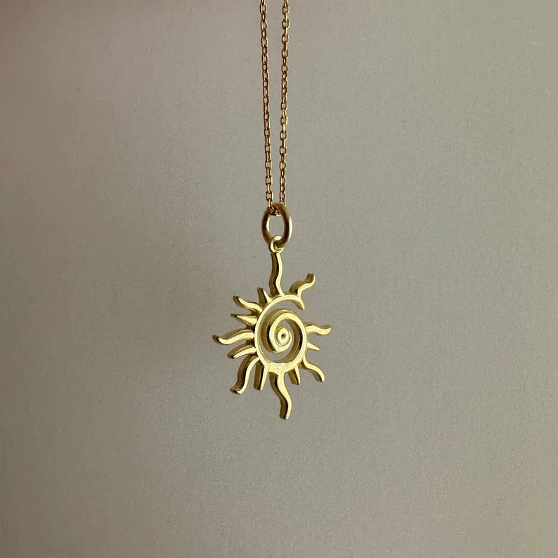 Gold sun-shaped pendant on a chain against a plain background