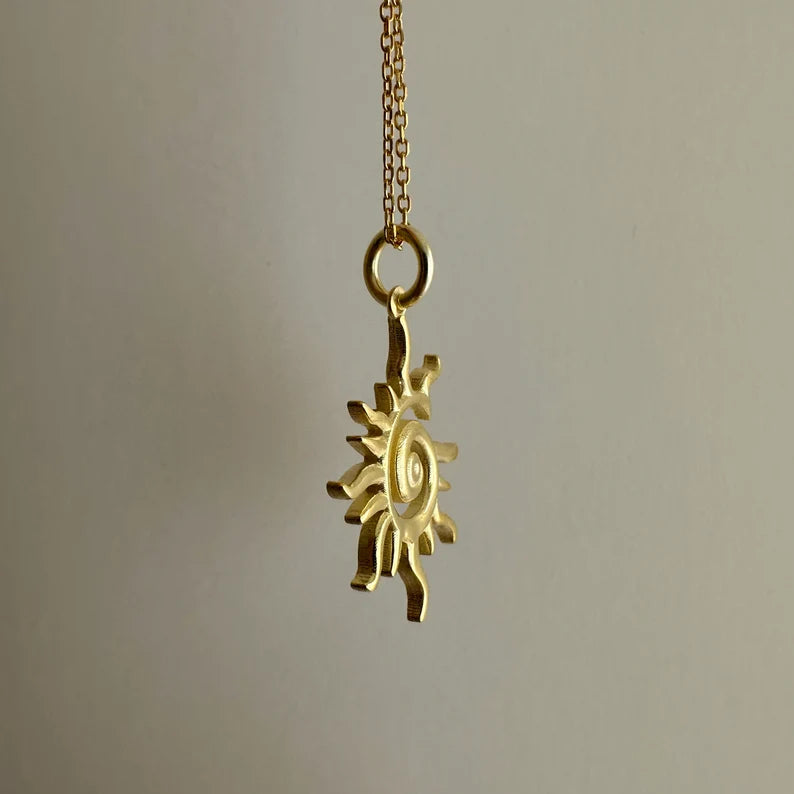 Gold sun-shaped pendant on a chain against a neutral background