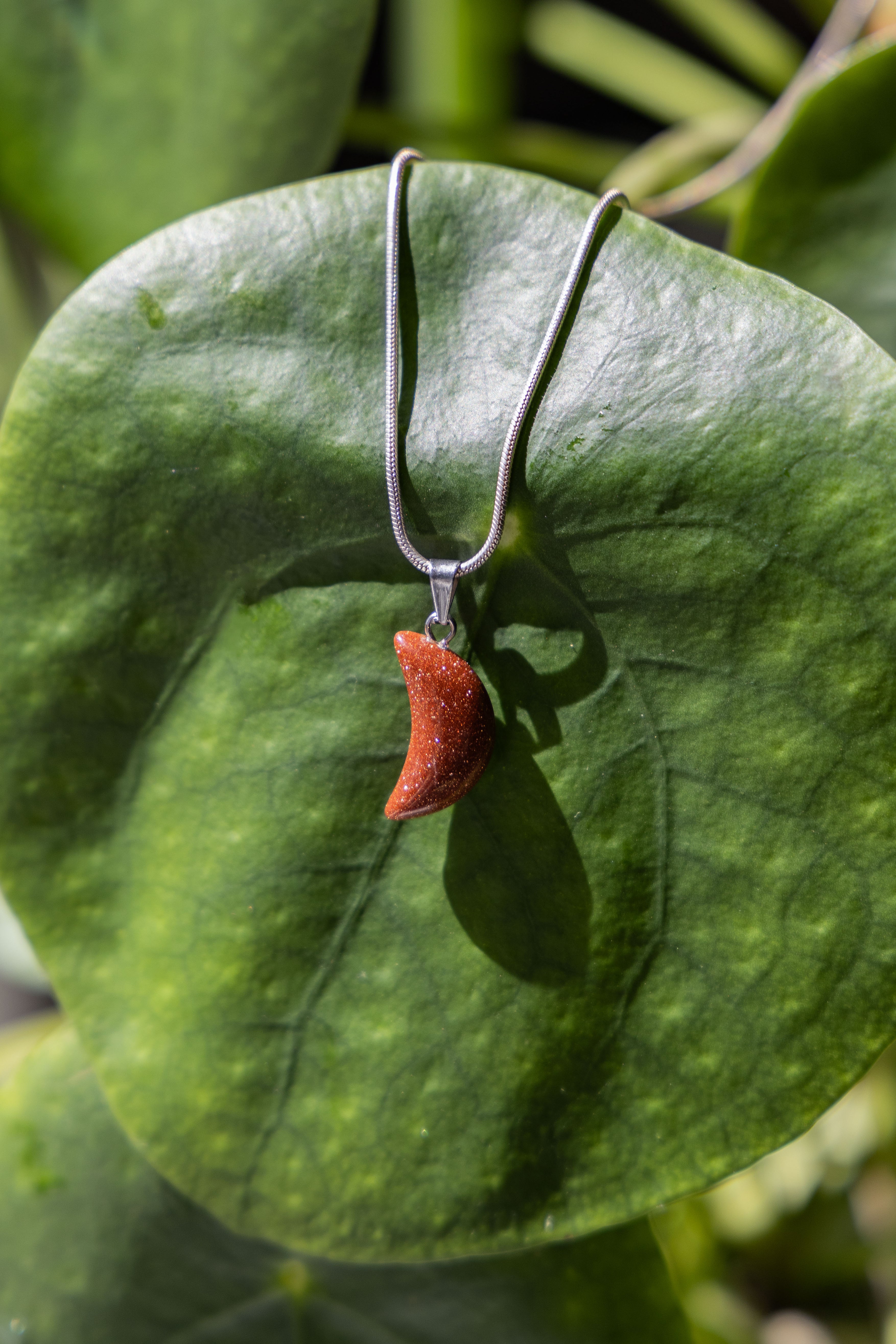 A sparkle-colored moon-shaped pendant necklace resting on a green leaf.