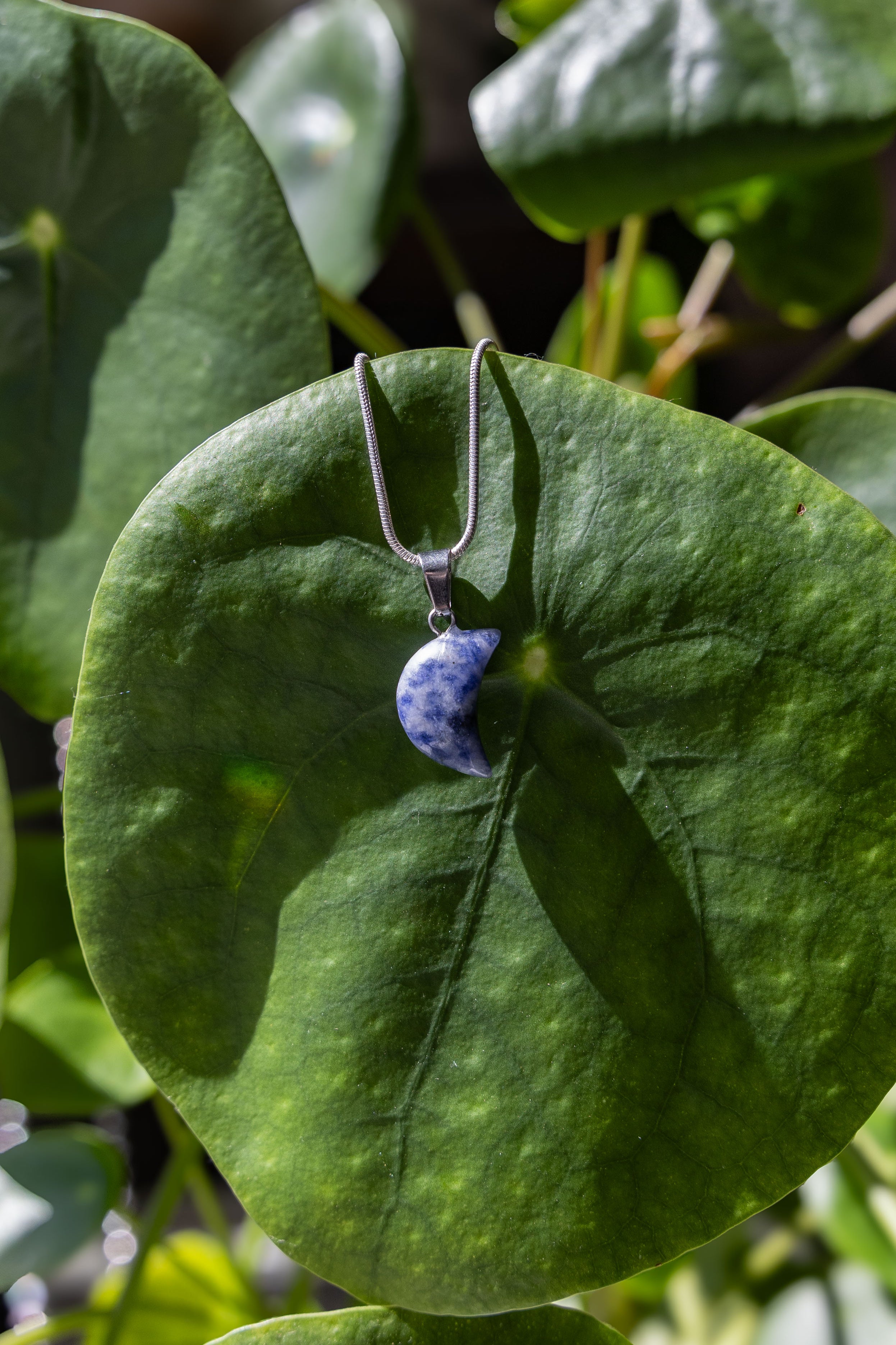 This image captures an enchanting view of the Moon Necklaces, a pair of elegant earrings featuring crystal half moon pendants. The pendants, showcased against a backdrop of intricately patterned blue and white tiles, sparkle beautifully, reflecting light and adding a touch of whimsy to the display.