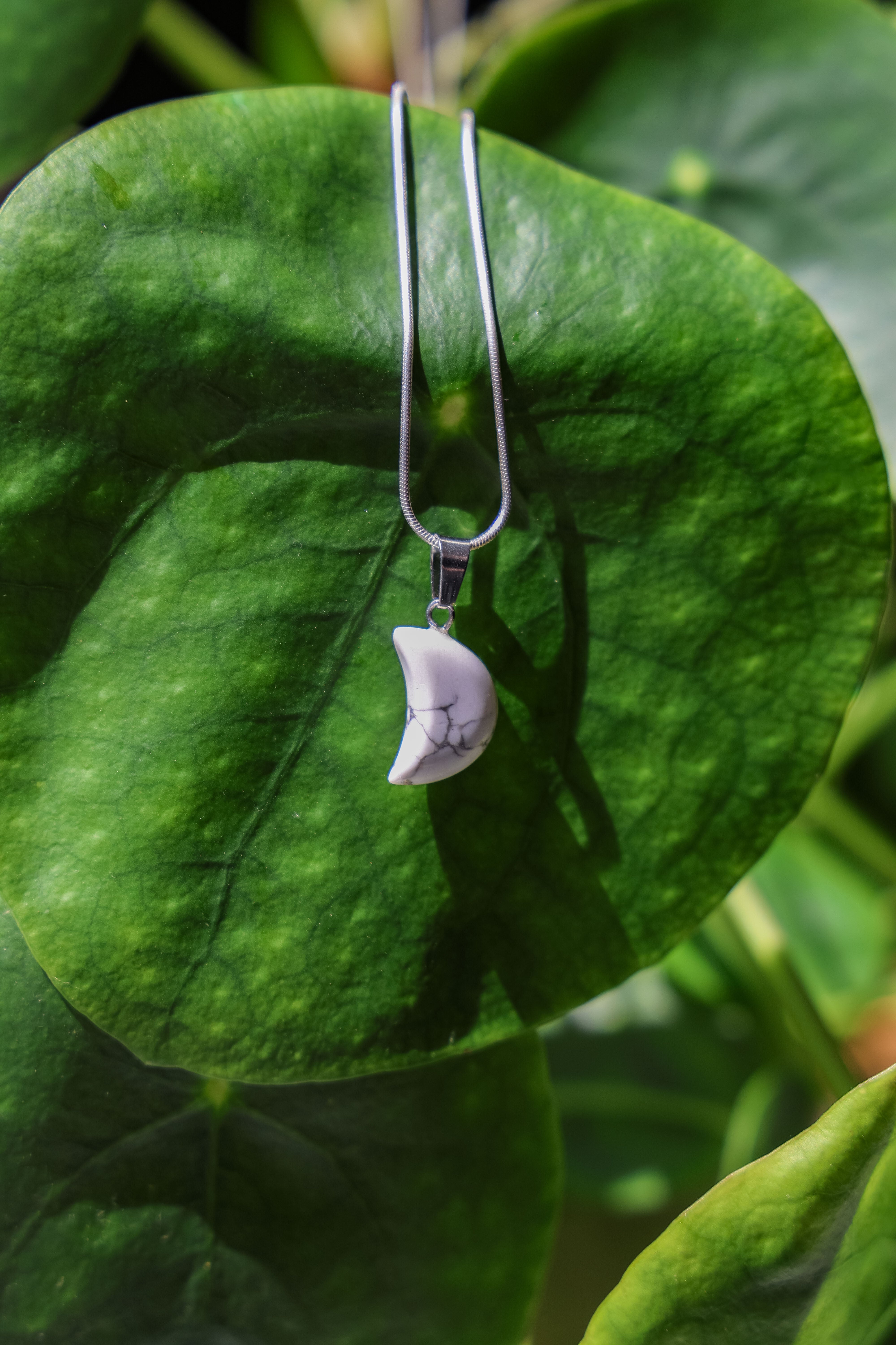 This image captures an enchanting view of the Moon Necklaces, a pair of elegant earrings featuring crystal half moon pendants. The pendants, showcased against a backdrop of intricately patterned blue and white tiles, sparkle beautifully, reflecting light and adding a touch of whimsy to the display.