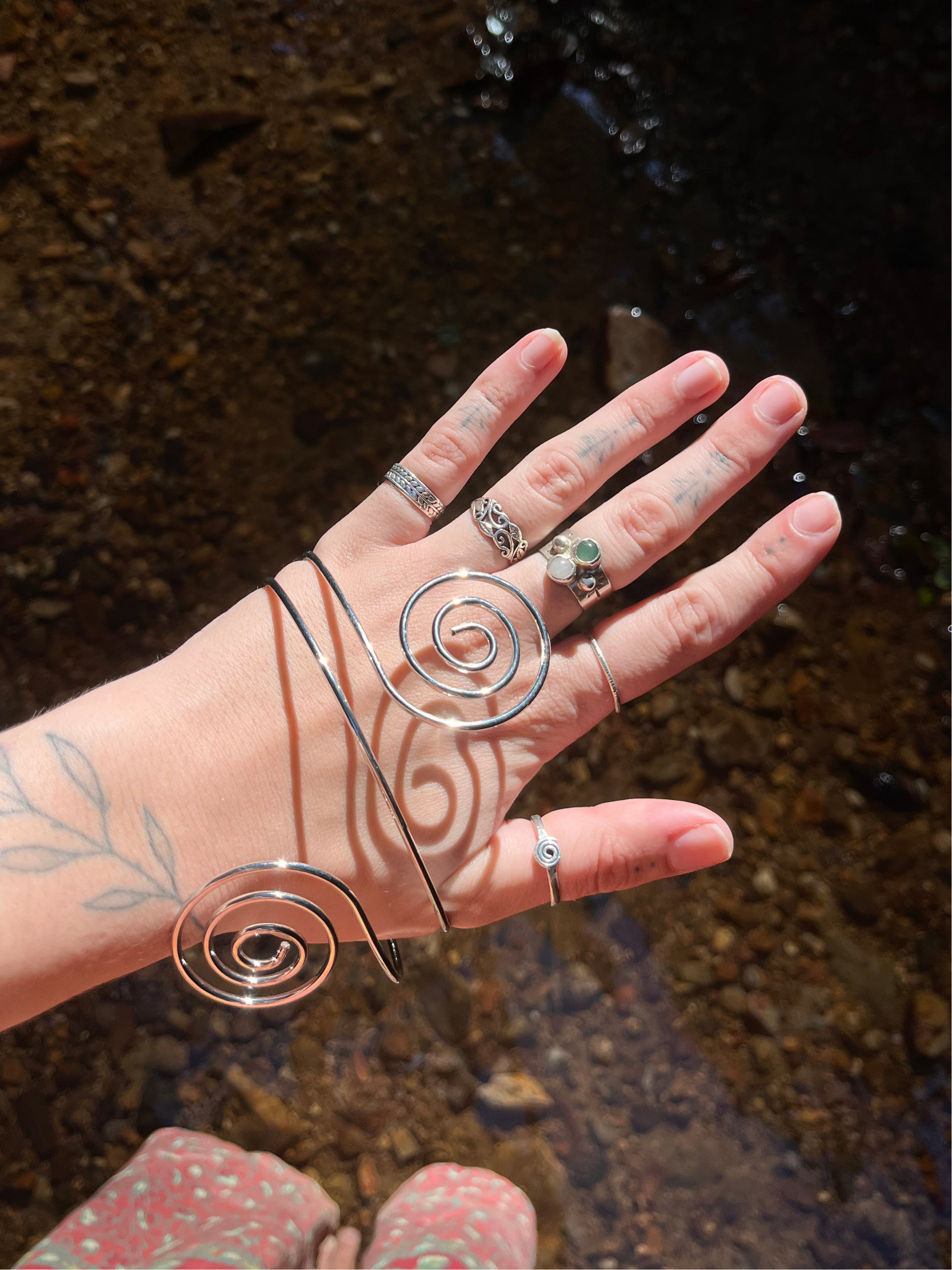 Silver spiral arm cuff held by a hand with a blurred natural background