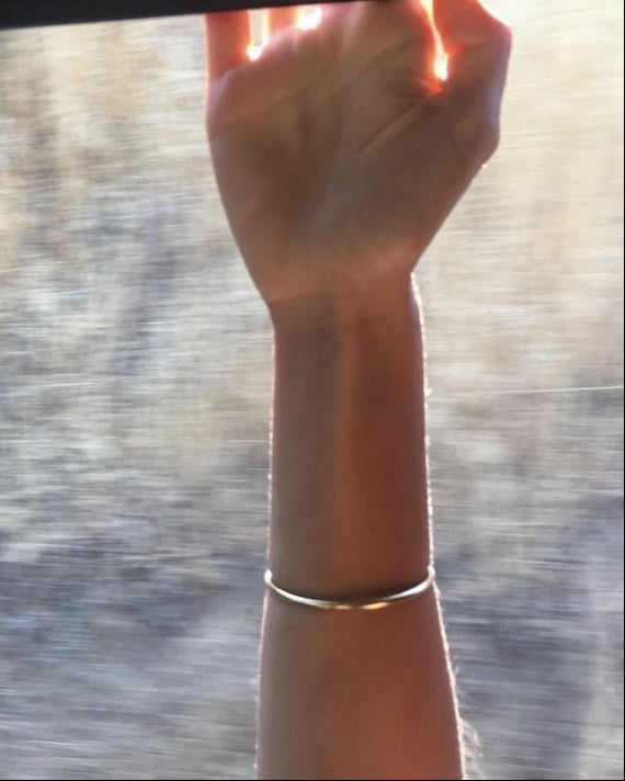 Hand with a bracelet reaching out of a window with a blurred outdoor background