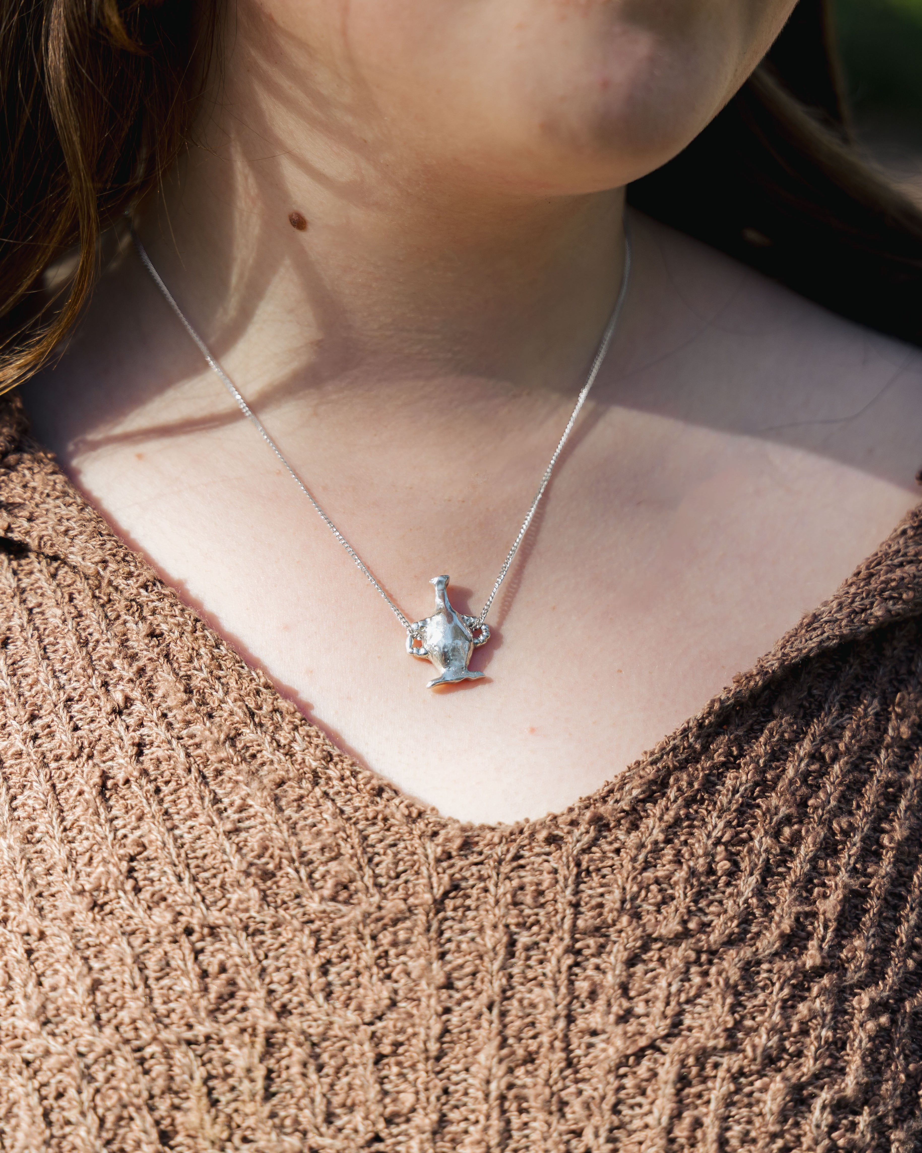 Close-up of a vase pendant on a necklace against a textured brown background