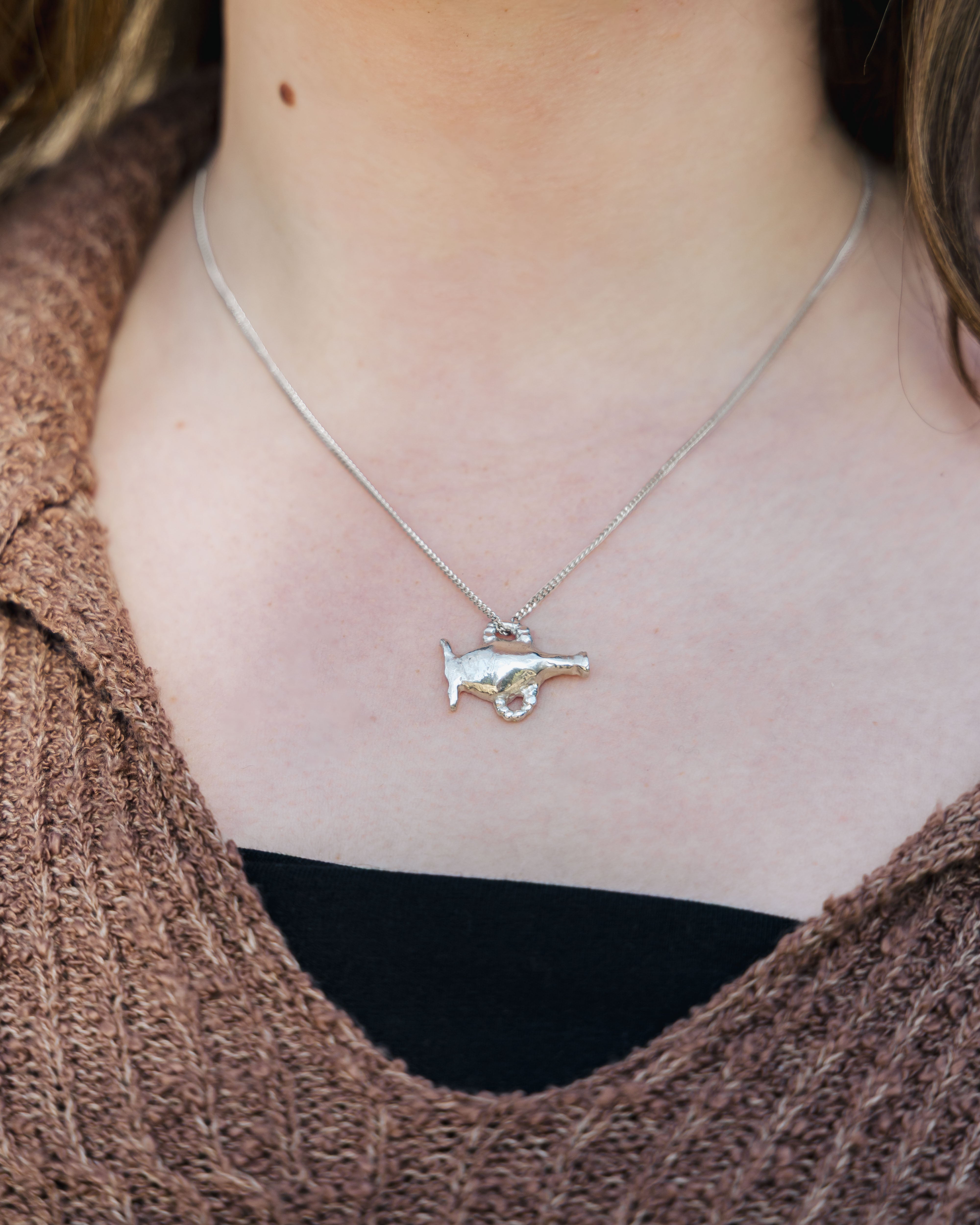 Close-up of a delicate silver necklace with a vase pendant worn by a person.