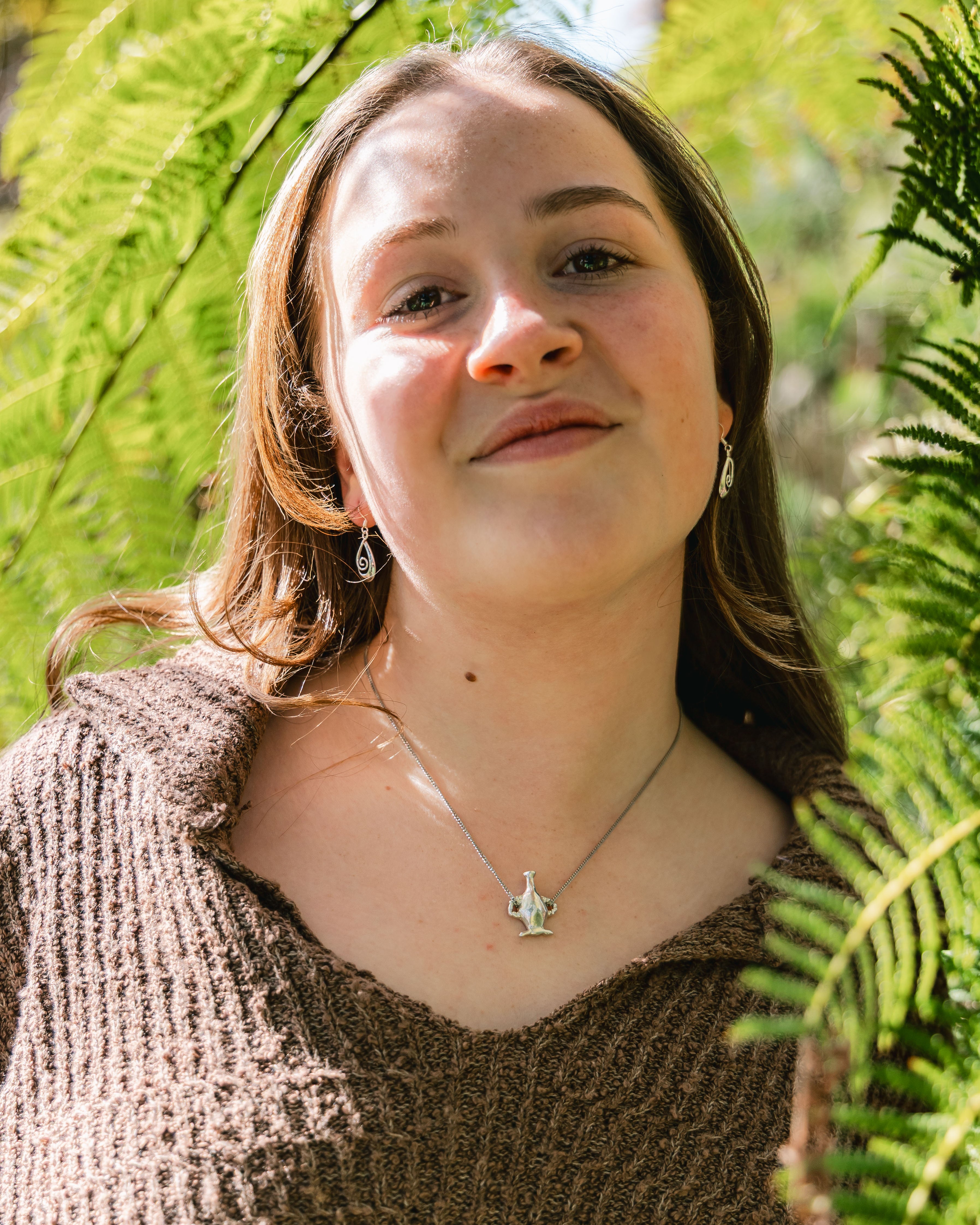 Close-up of a vase pendant on a necklace against a textured brown background