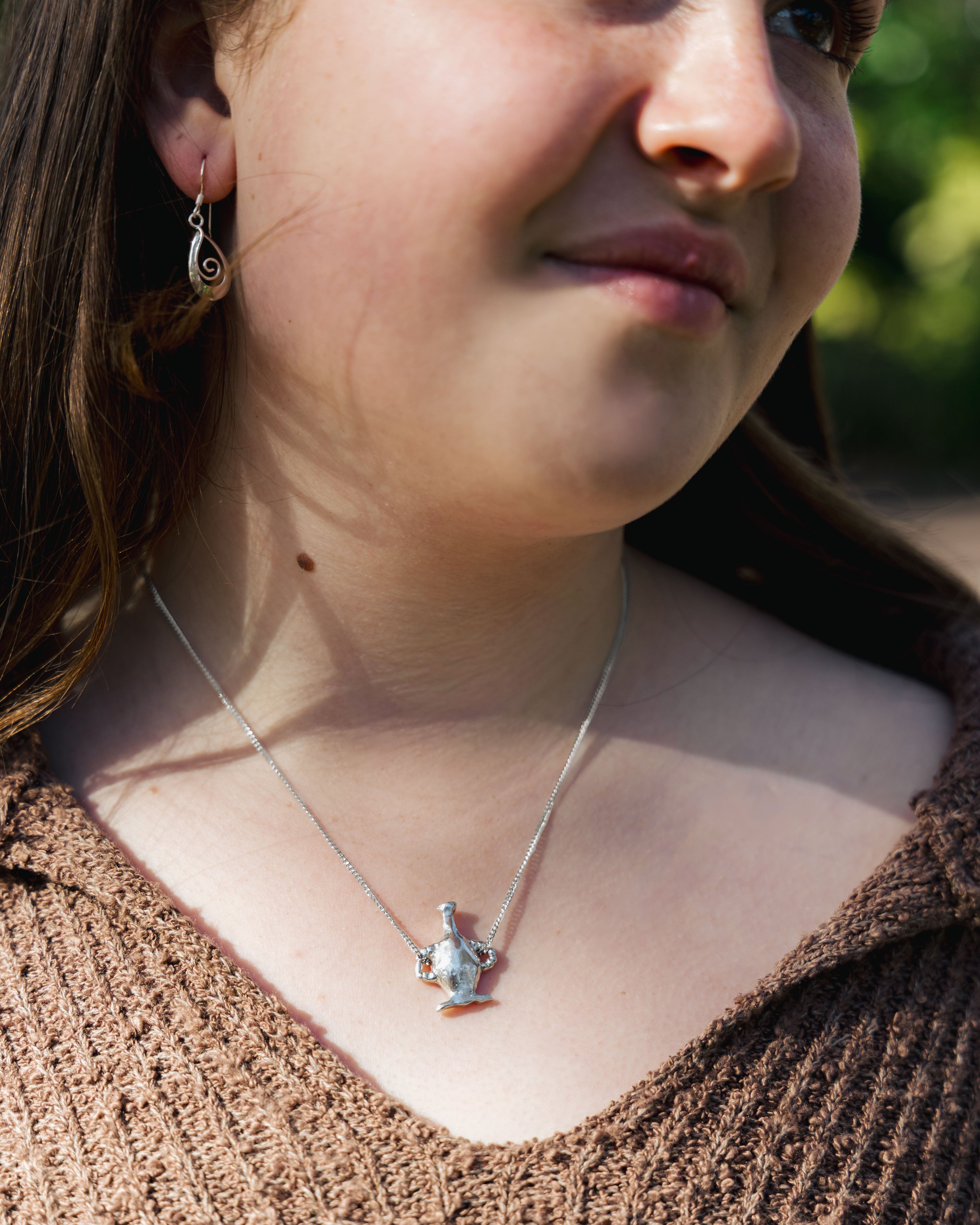 Close-up of a person wearing a vase pendant necklace with a blurred background