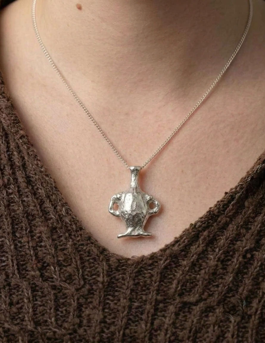 Silver trophy-shaped pendant on a necklace worn by a person in a brown sweater.