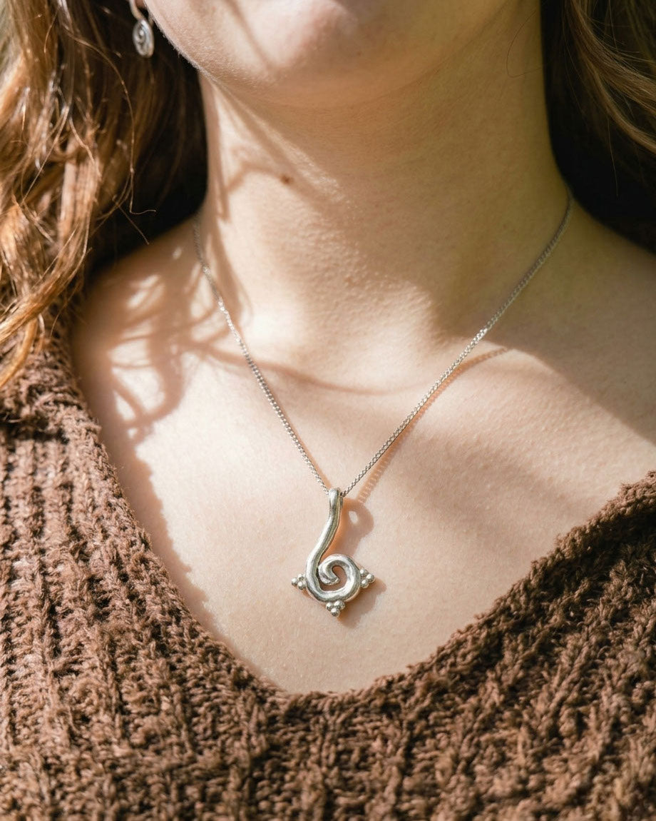 Close-up of a person wearing a silver necklace with a decorative pendant.