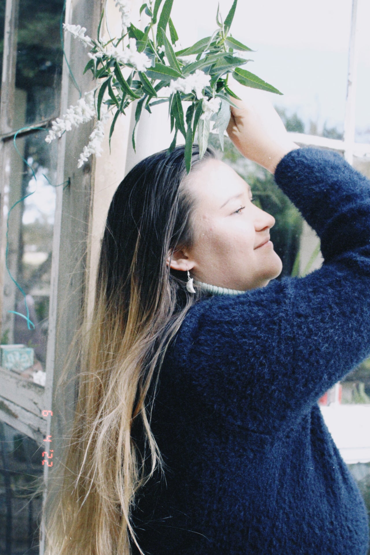 Woman wearing crystal crescent moon earrings holding a plant against a blurred outdoor background