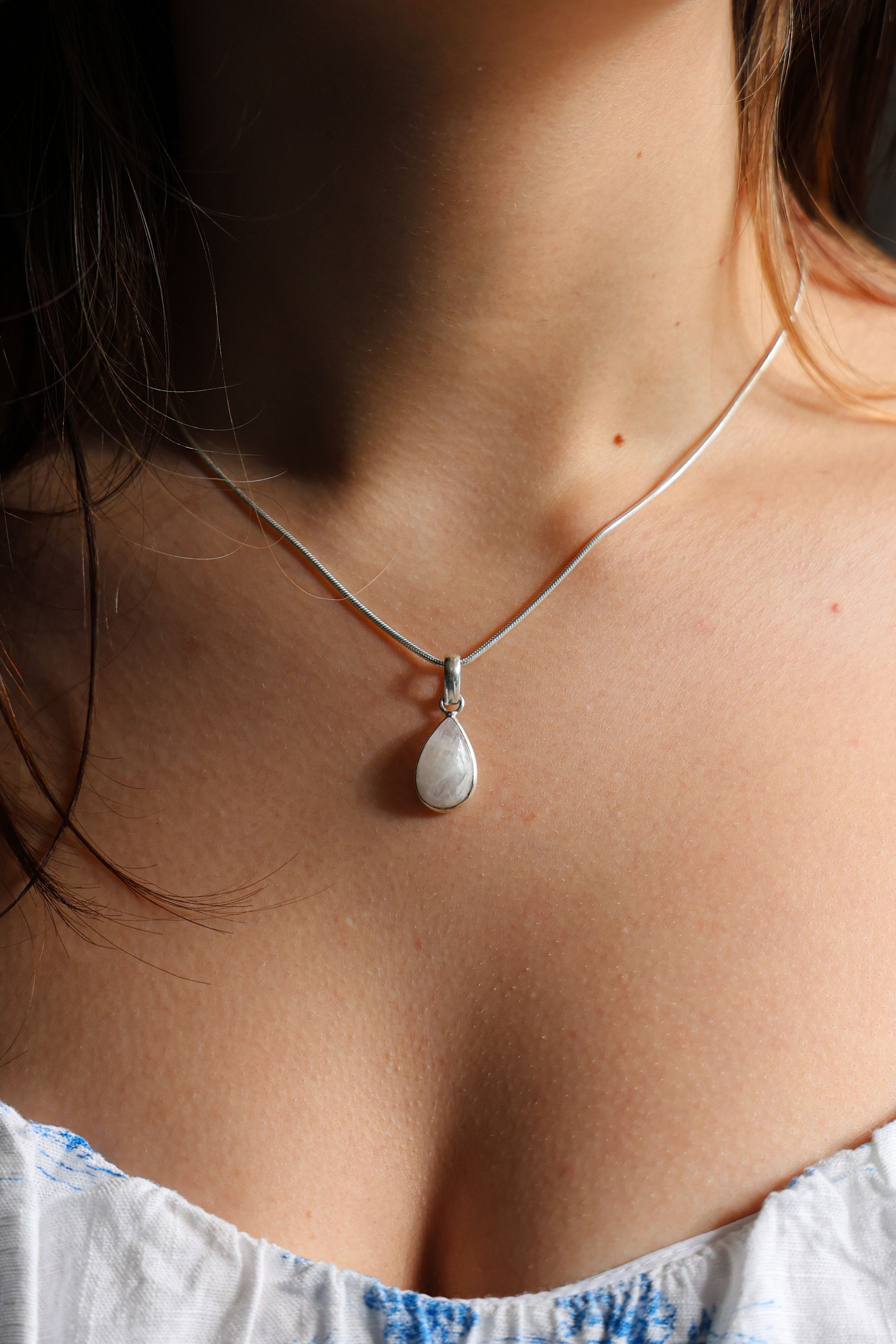 A person wearing a sterling silver necklace with a teardrop-shaped moonstone pendant.