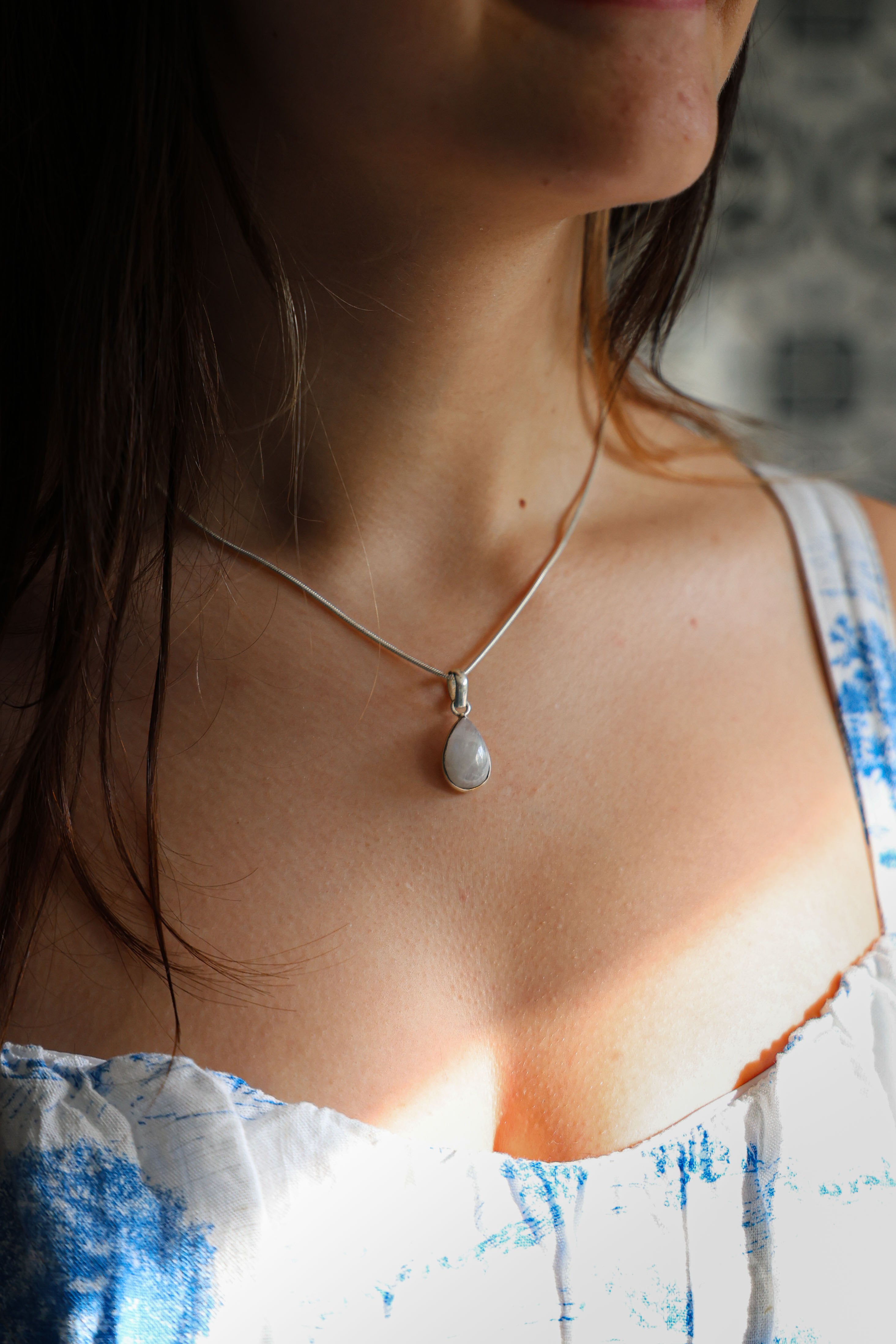 A person wearing a sterling silver necklace with a teardrop-shaped moonstone pendant.